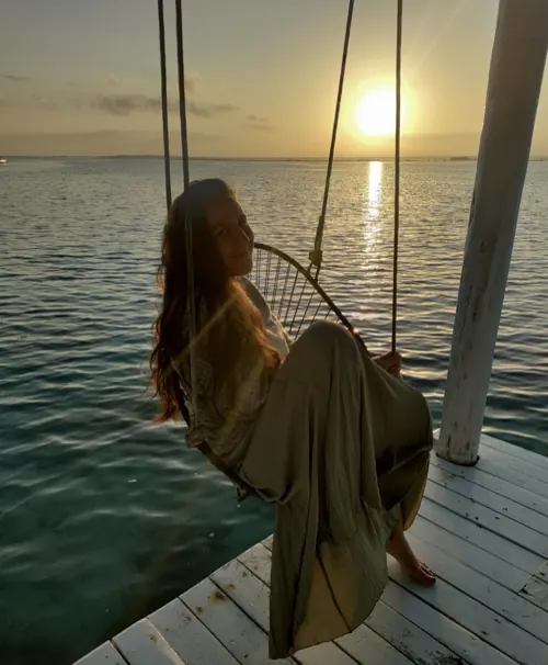 Jasina Ouahid bei Sonnenuntergang auf einer Schaukel über dem Wasser